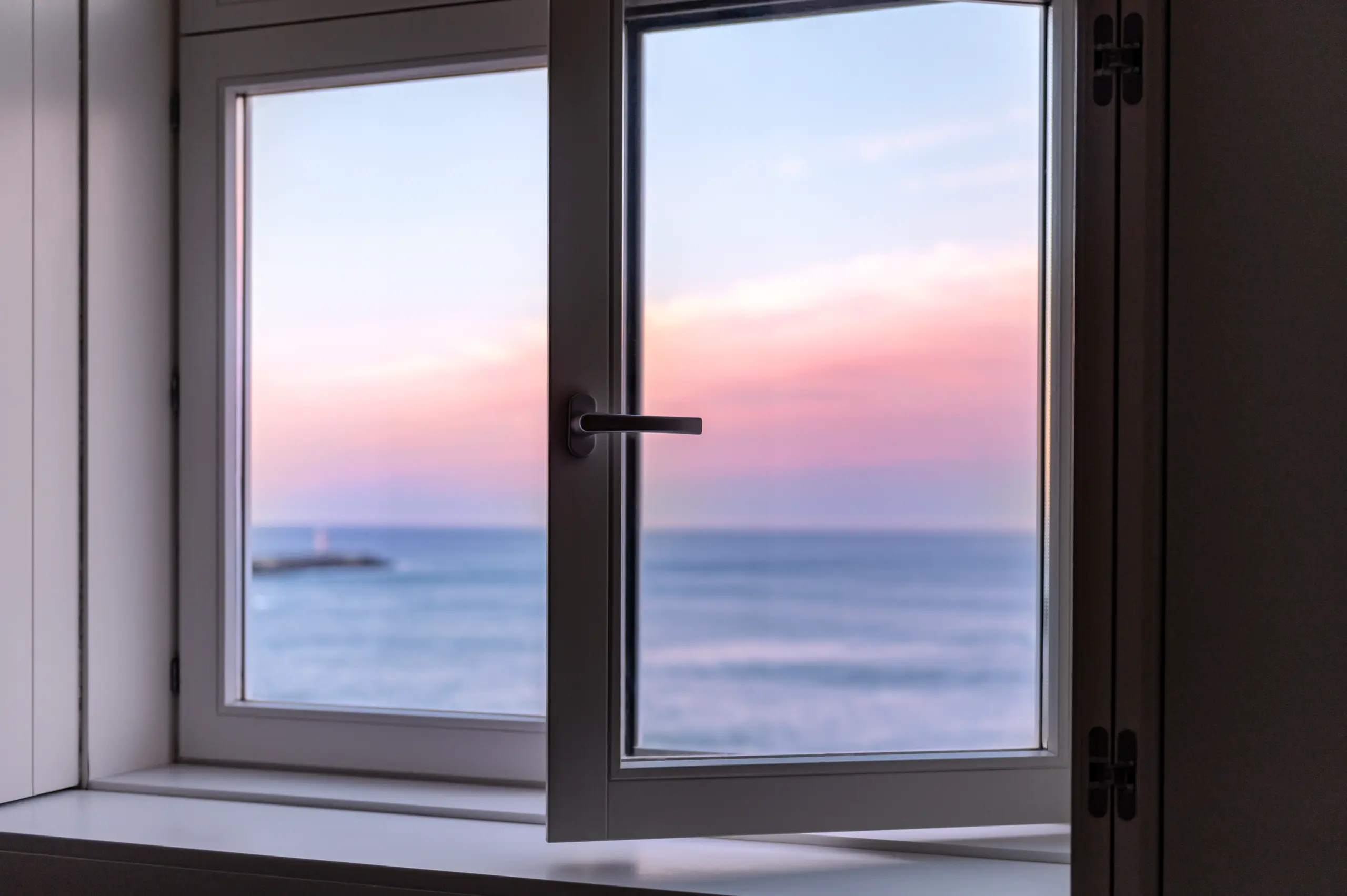 A view of the sea through a partially open window, showcasing a sunset sky