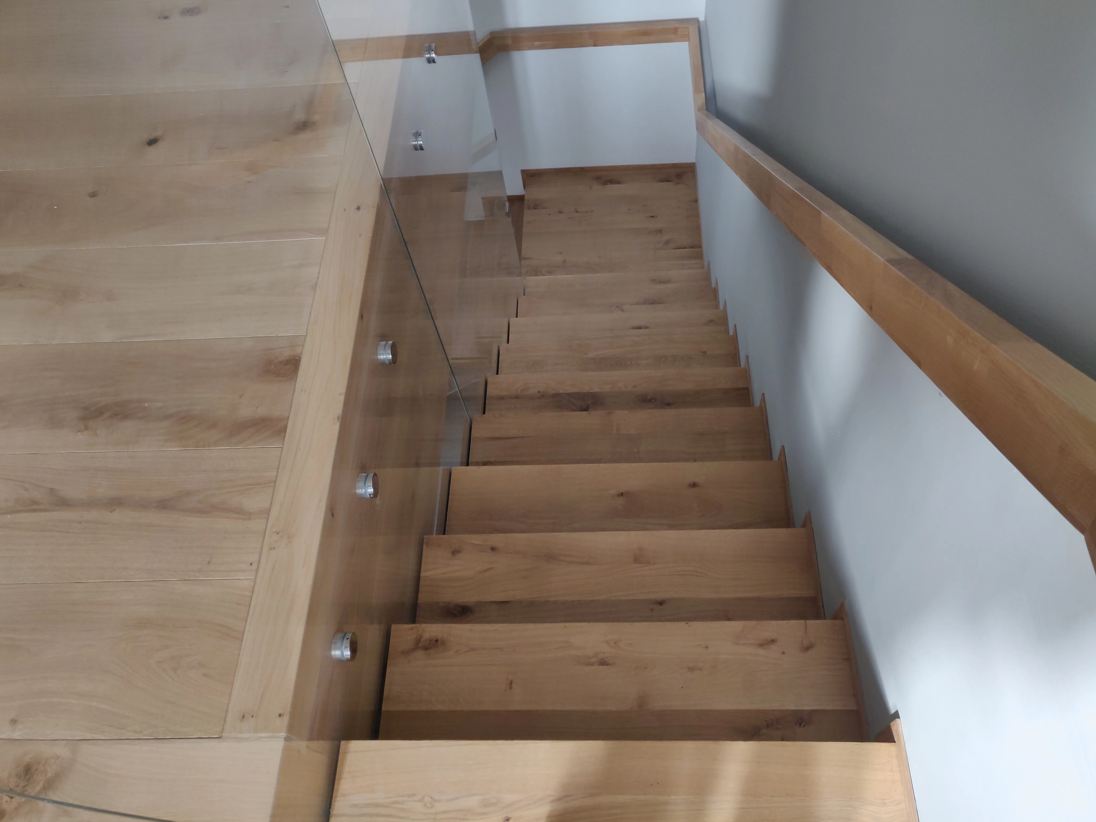 Oak stairs with glass railing leading downwards in a modern interior