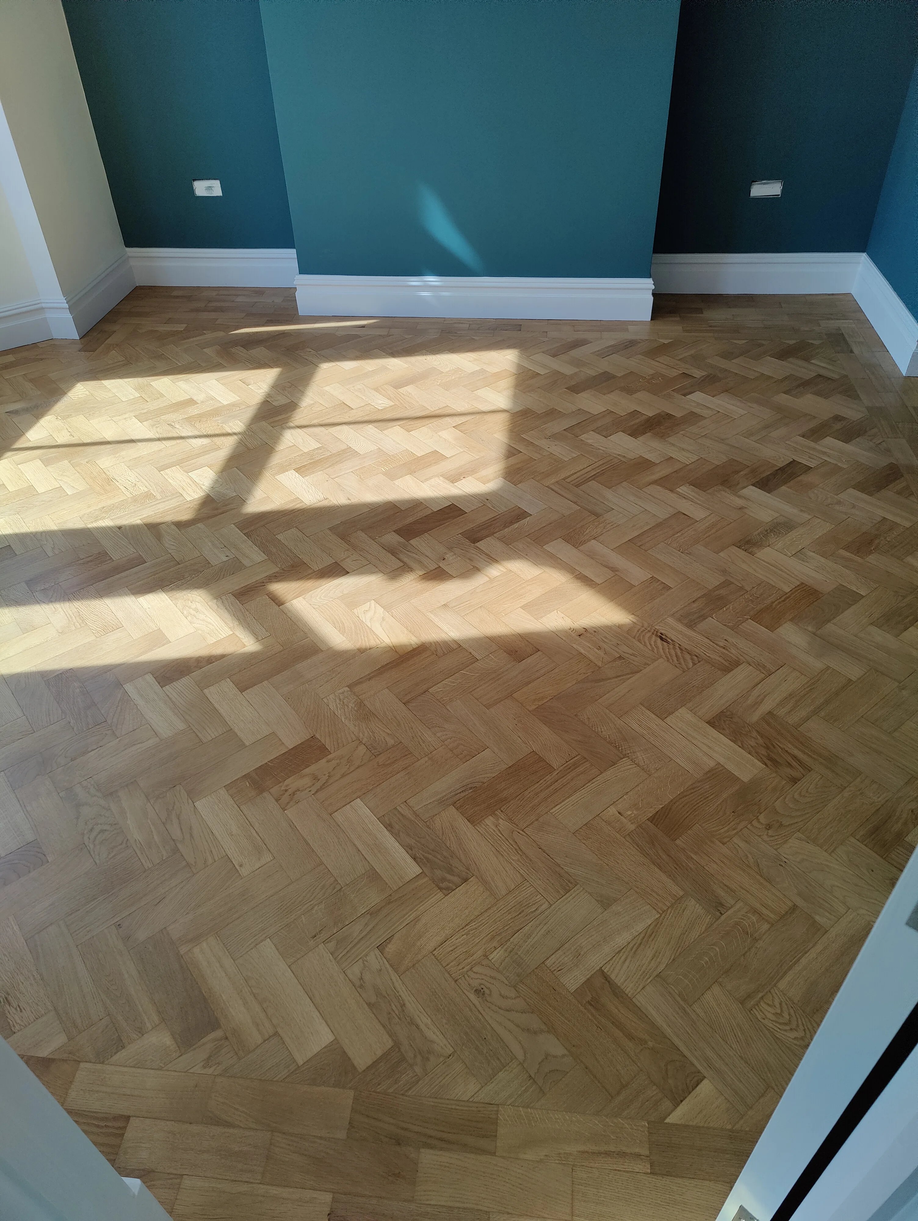 A well-finished parquet flooring in a newly refurbished room with sunlight streaming in
