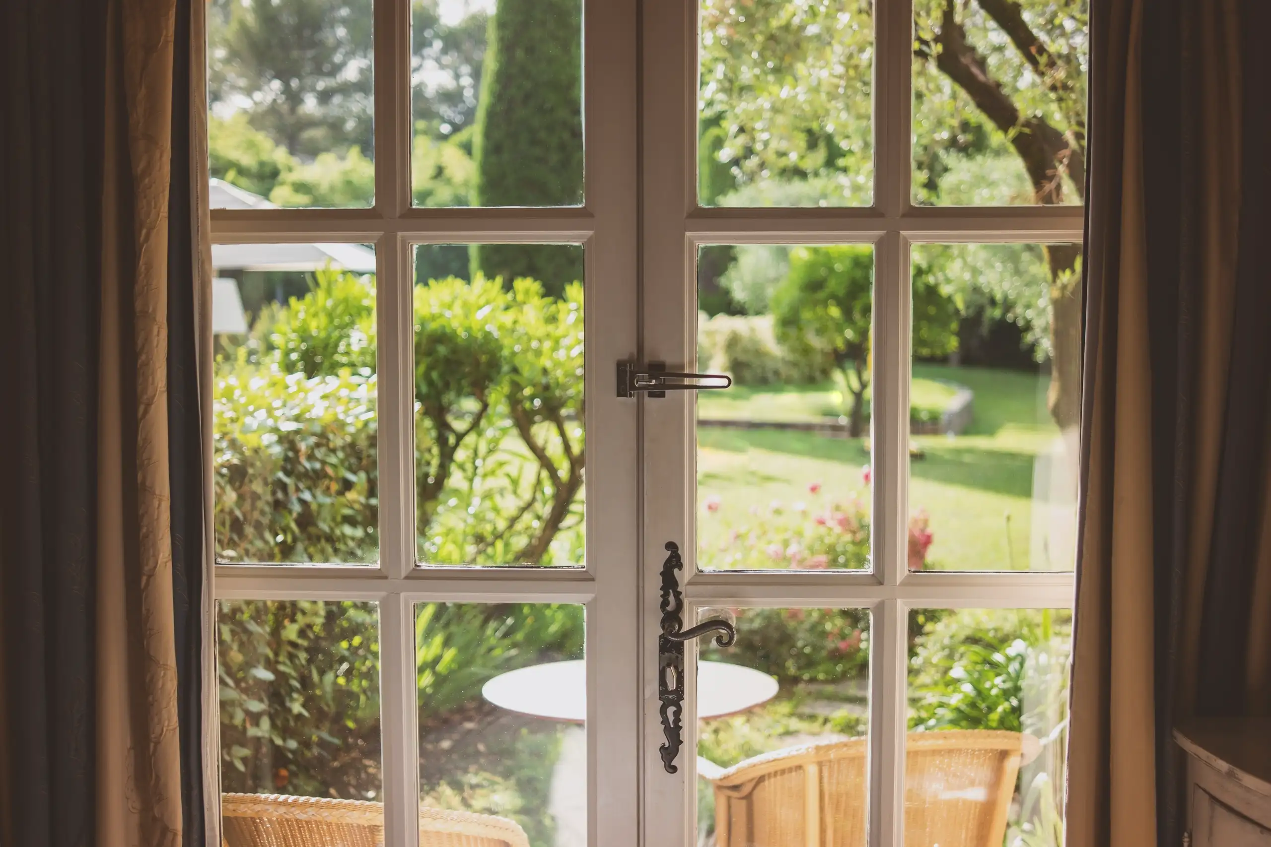 View through a white-framed window showcasing a garden with green plants and outdoor seating
