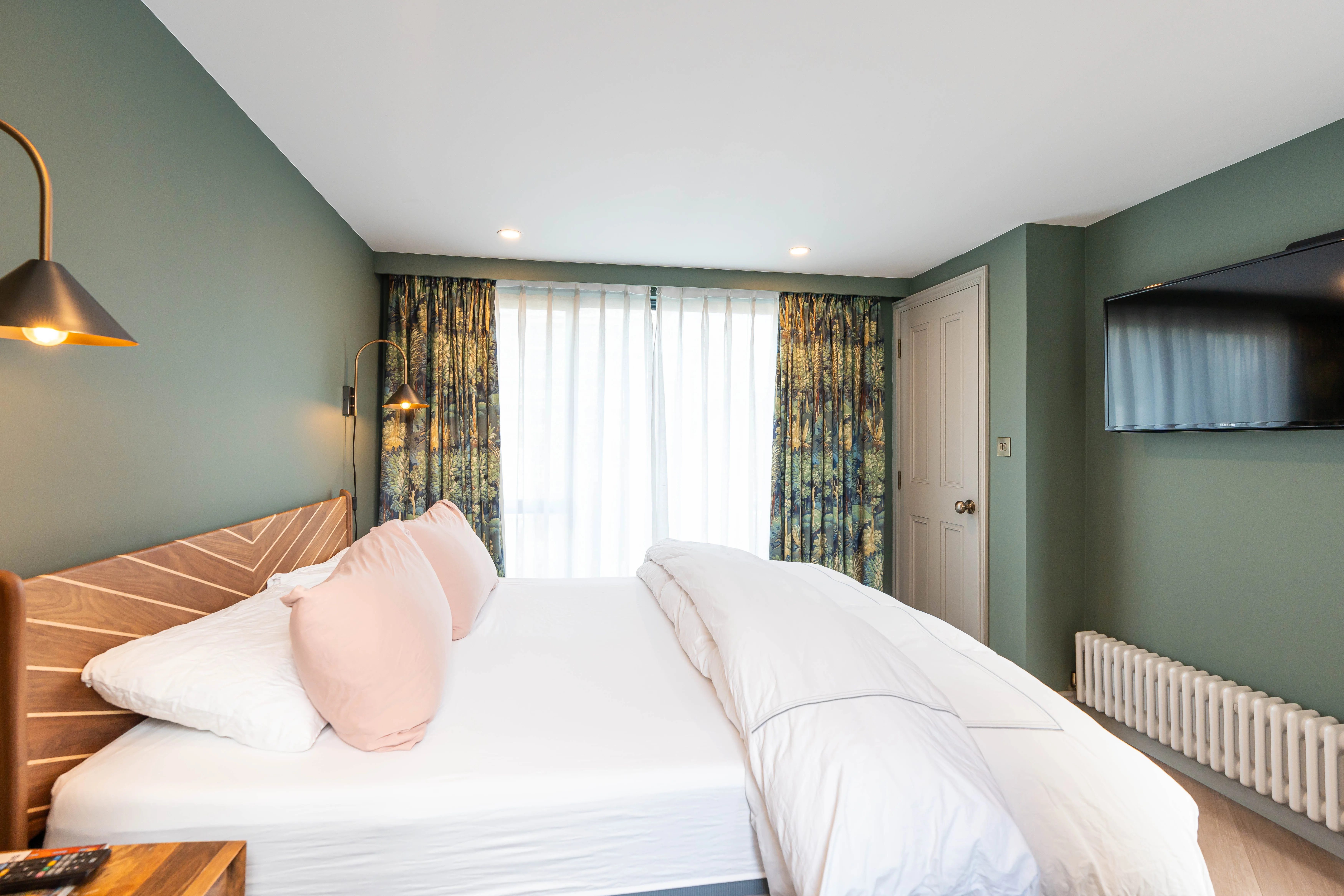 Modern bedroom with a double bed, decorative pillows, and large windows featuring elegant curtains