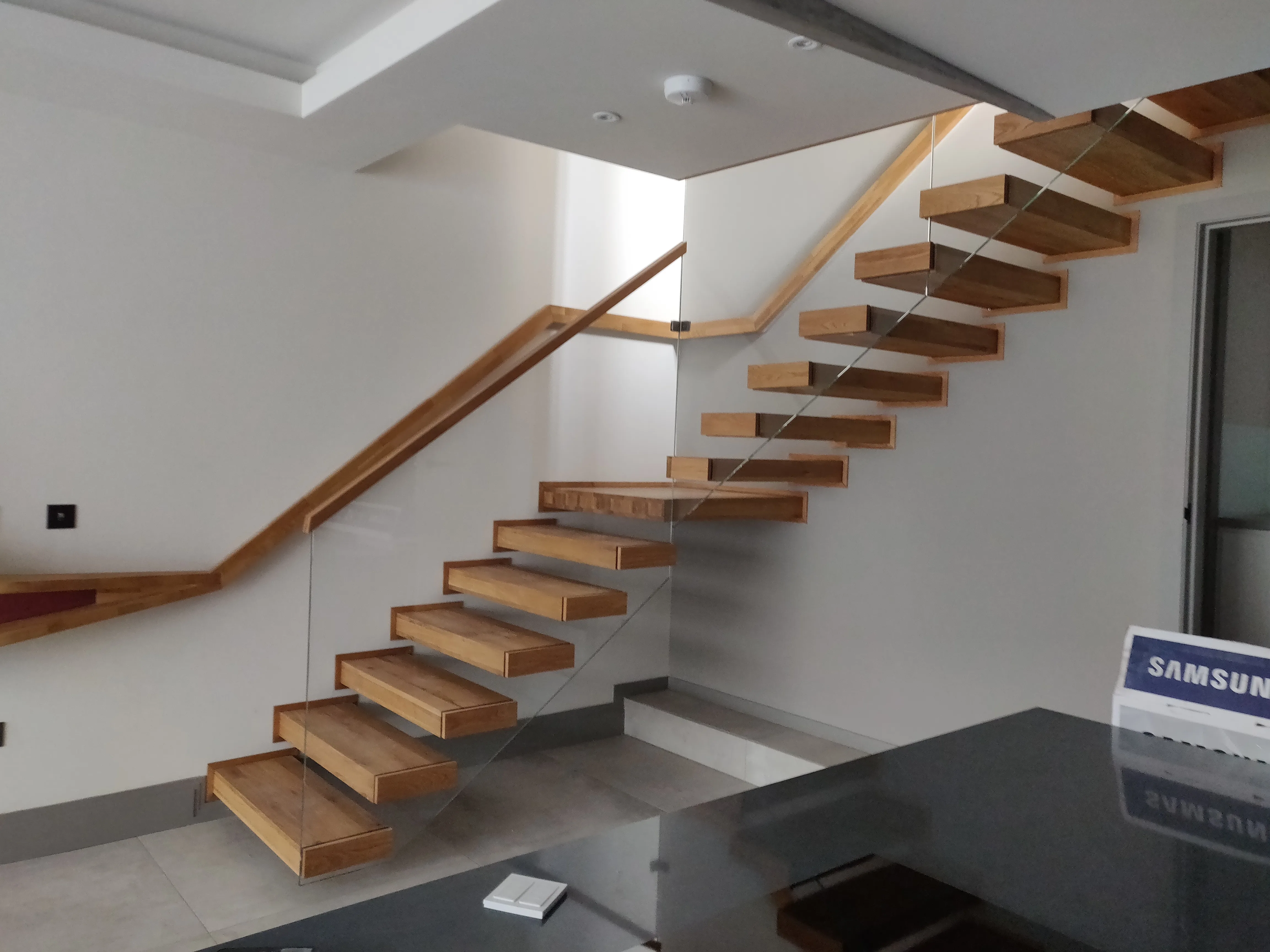 Modern floating staircase with wooden treads and glass railing in a well-lit interior
