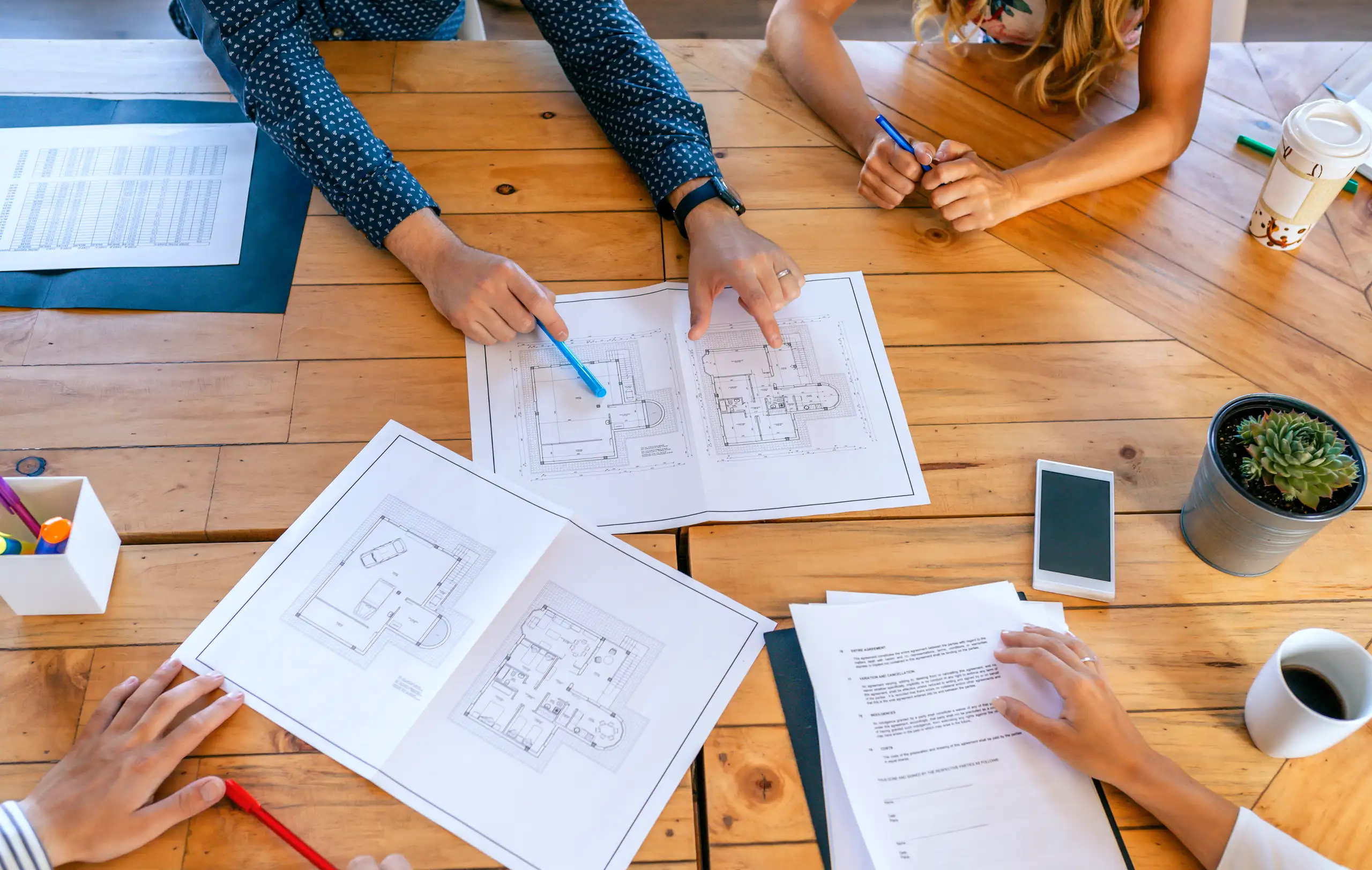 A group discussing home refurbishment plans over a wooden table with blueprints and notes