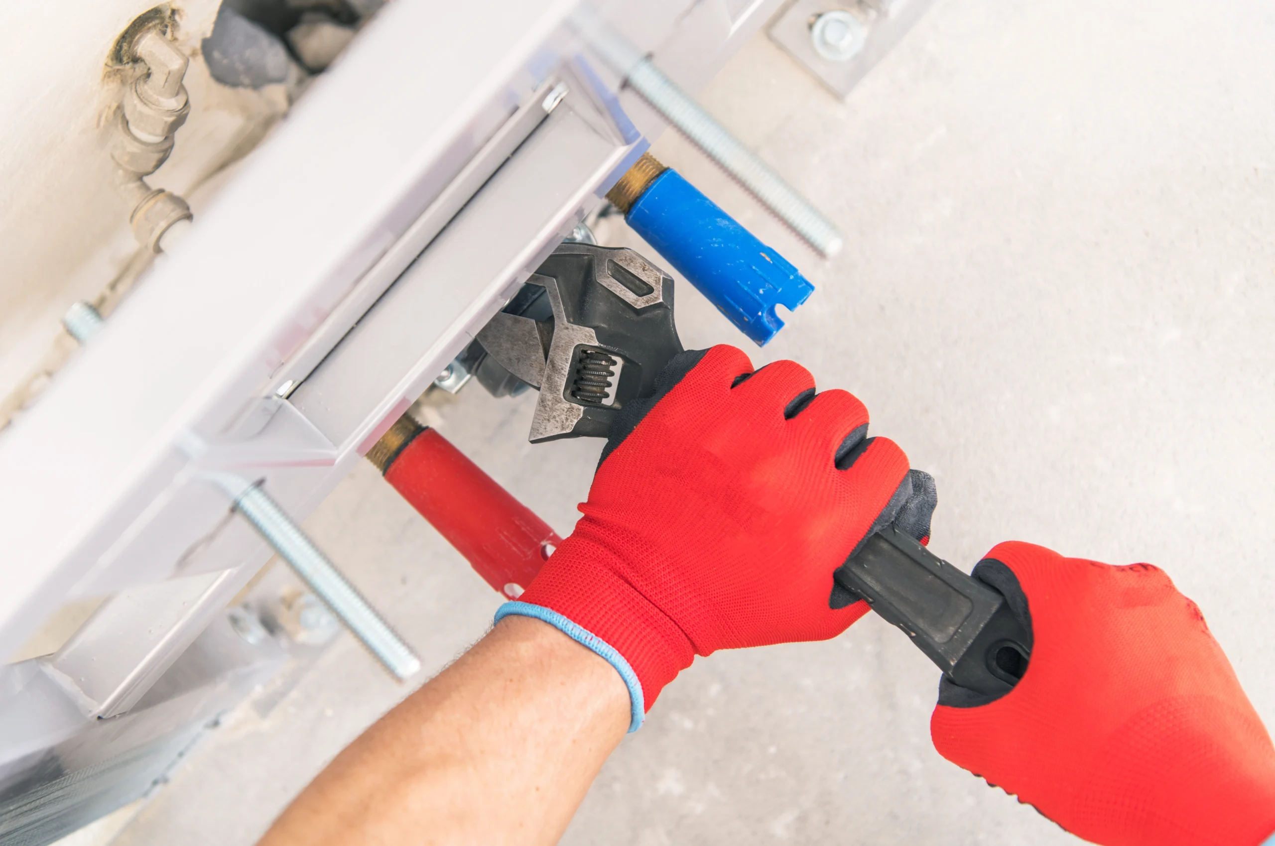 A person in red gloves using an adjustable wrench to tighten pipes during plumbing work