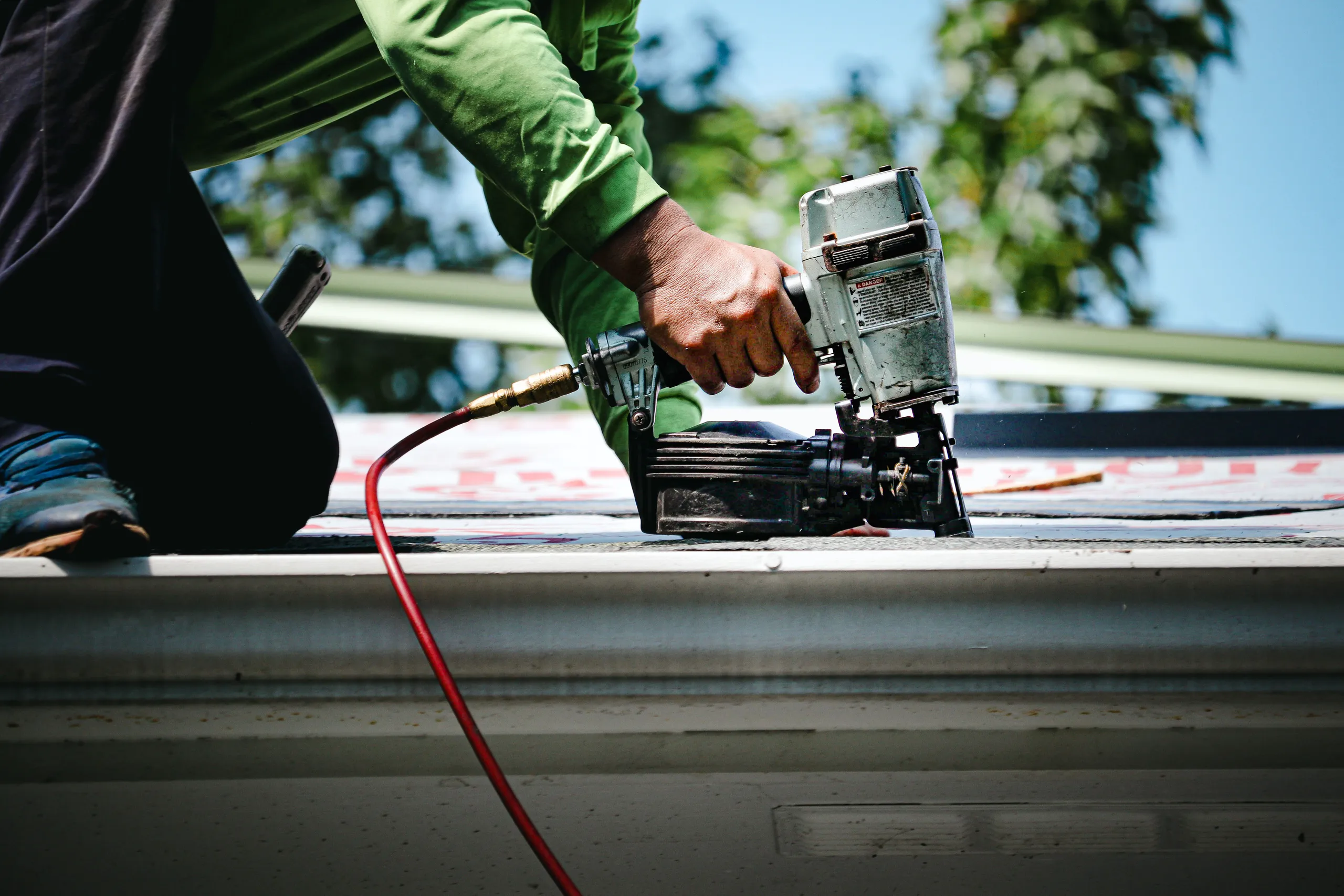 A worker using a pneumatic nail gun on a roof during a roof installation project