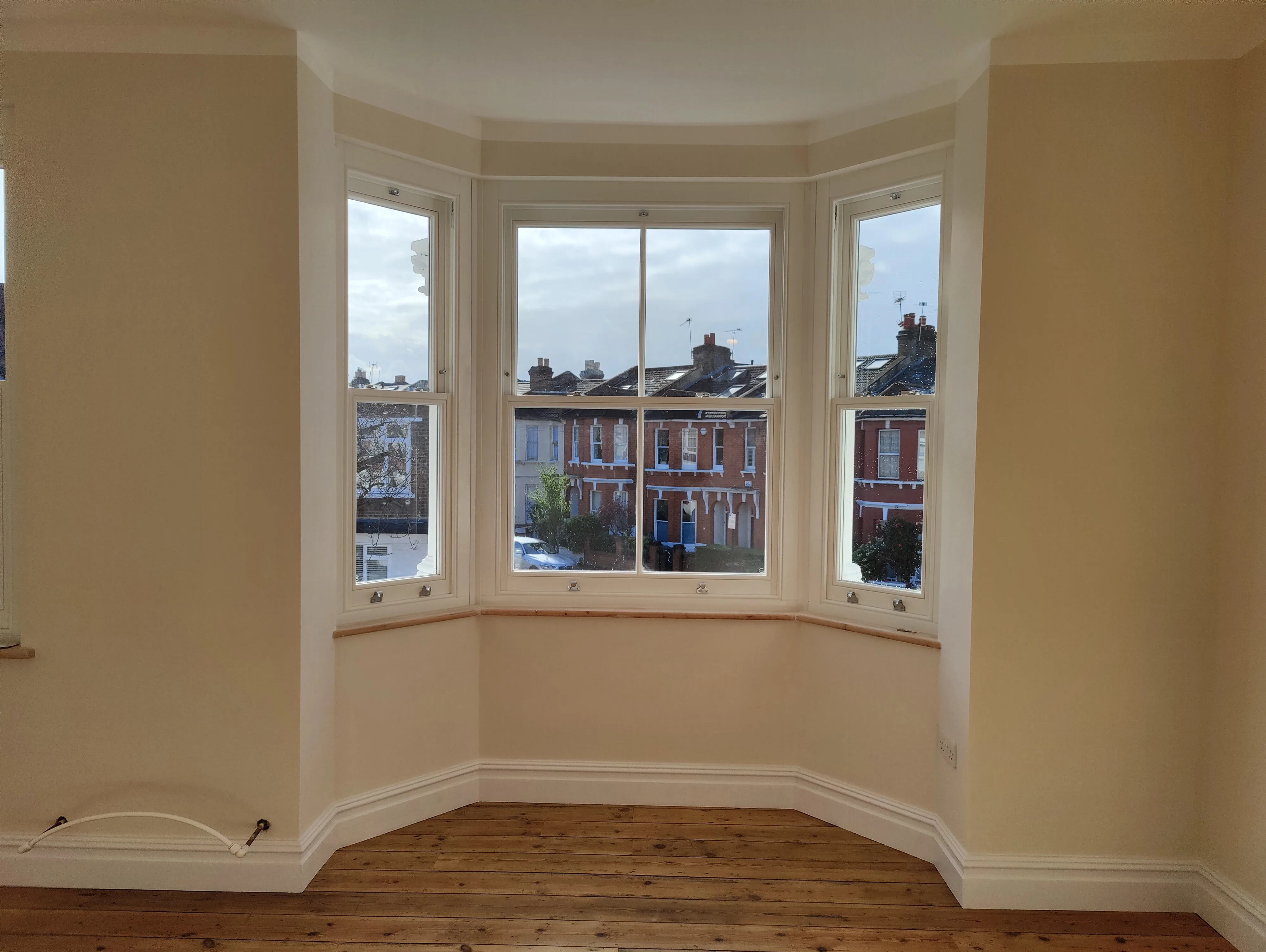 Bright room with large windows showcasing natural light and wooden flooring, suitable for home refurbishment