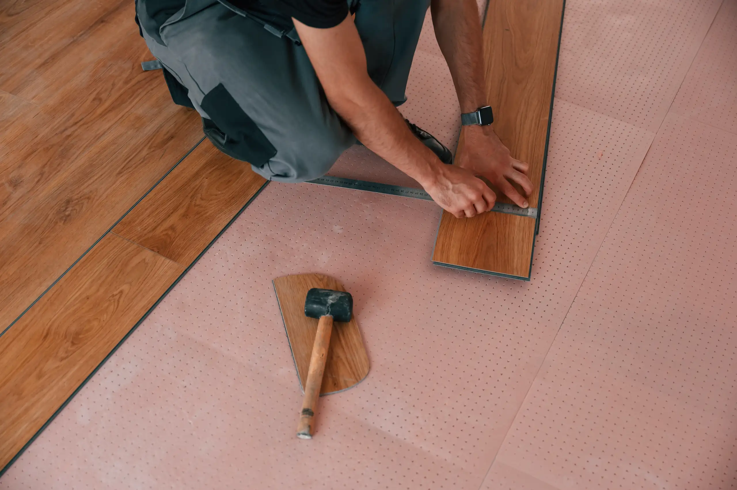 A worker installing wood flooring using a mallet and precision tools